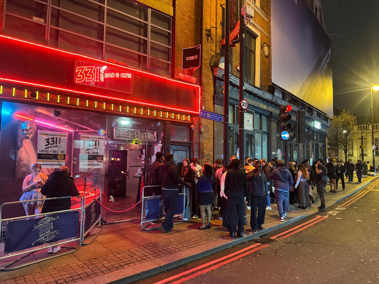 Crowd queuing outside the red neon 331 Old St Bar & Club front at night